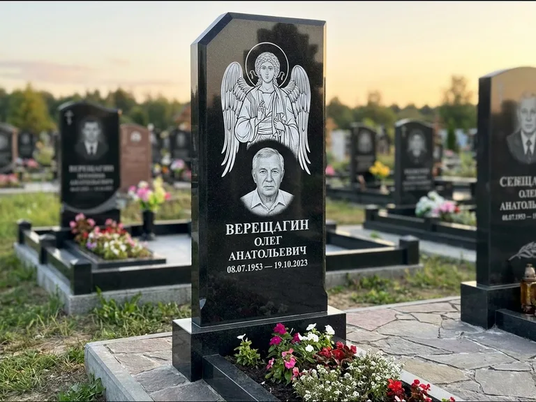 Памятник с гравировкой иконы: стела с резным навершием и нимбом в золоте — гравировка образа Спасителя, высокие разросшиеся туи полукругом, работа «Мельникова» в Ижевске