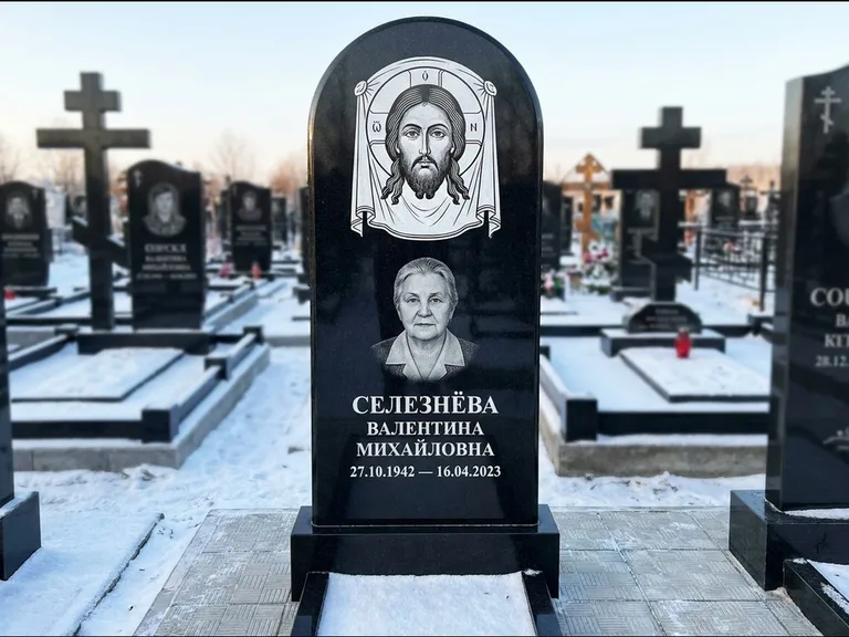 Памятник с гравировкой иконы: небольшая скромная одиночная стела с именной иконой — золочёный нимб на образе, аккуратный участок с газоном, работа «Ковалёв» в Ижевске