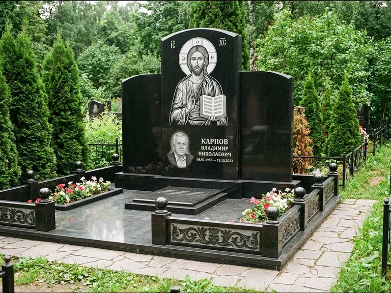 Памятник с гравировкой иконы: широкая панорамная стела с золочёным нимбом — гравировка образа Матроны Московской, цветник с белыми хризантемами, работа «Мельникова» в Ижевске