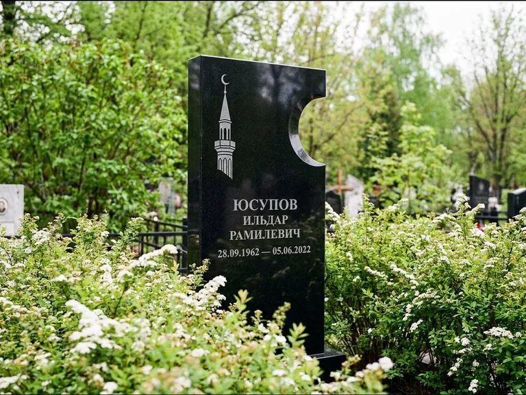 Мусульманский памятник с гравировкой мечети: стела с боковым вырезом в форме полумесяца — гравировка минарета с полумесяцем, низкие кусты спиреи в цвету, работа «Юсупов» в Ижевске